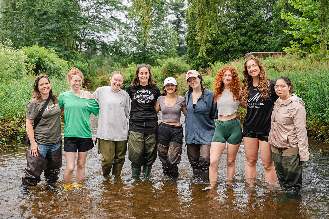 A group of college students and a professor stands together in a creek